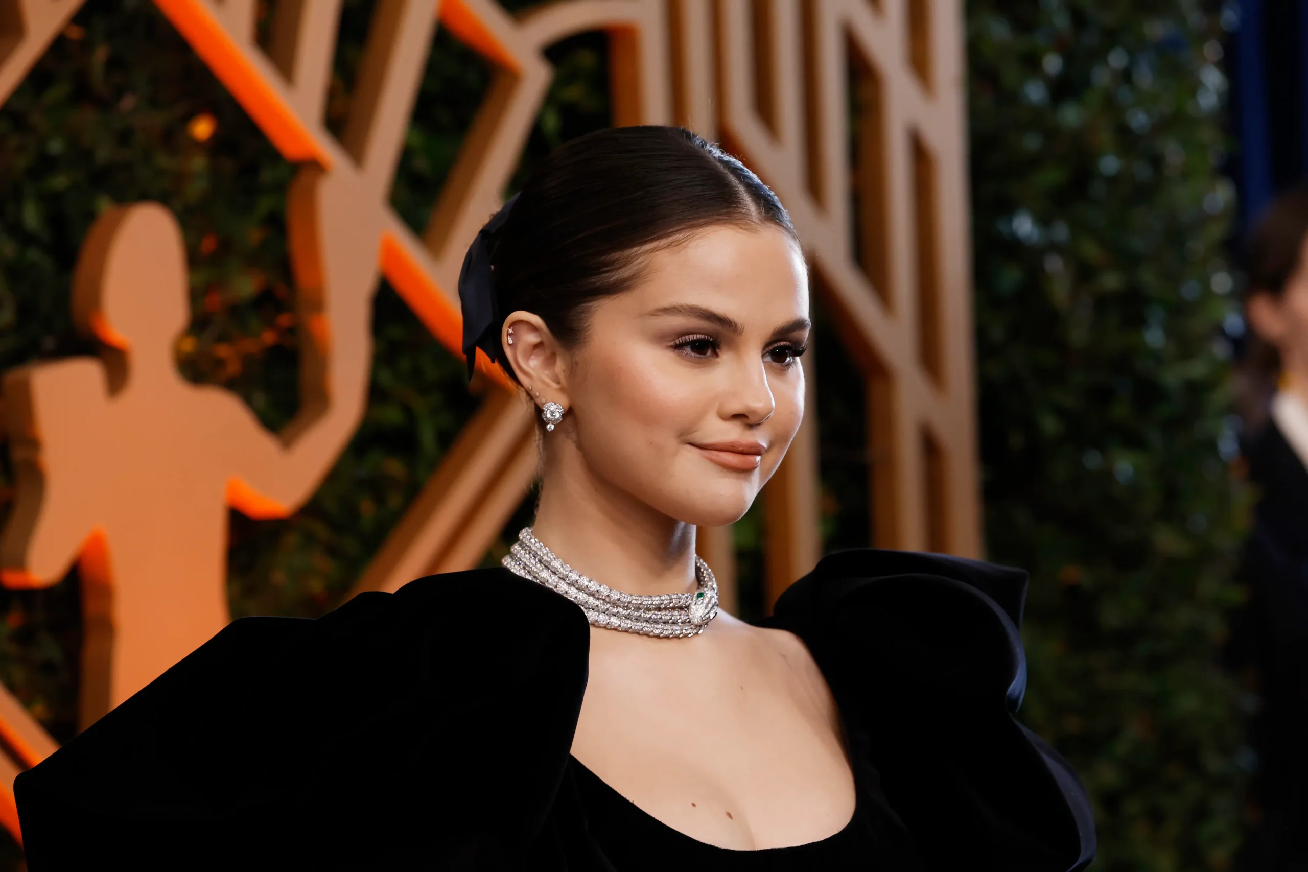 A woman in an elegant black dress and sparkling jewelry is posing on the red carpet.
