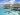 An aerial view of a couple standing on a jetty by overwater bungalows in a clear blue ocean setting.