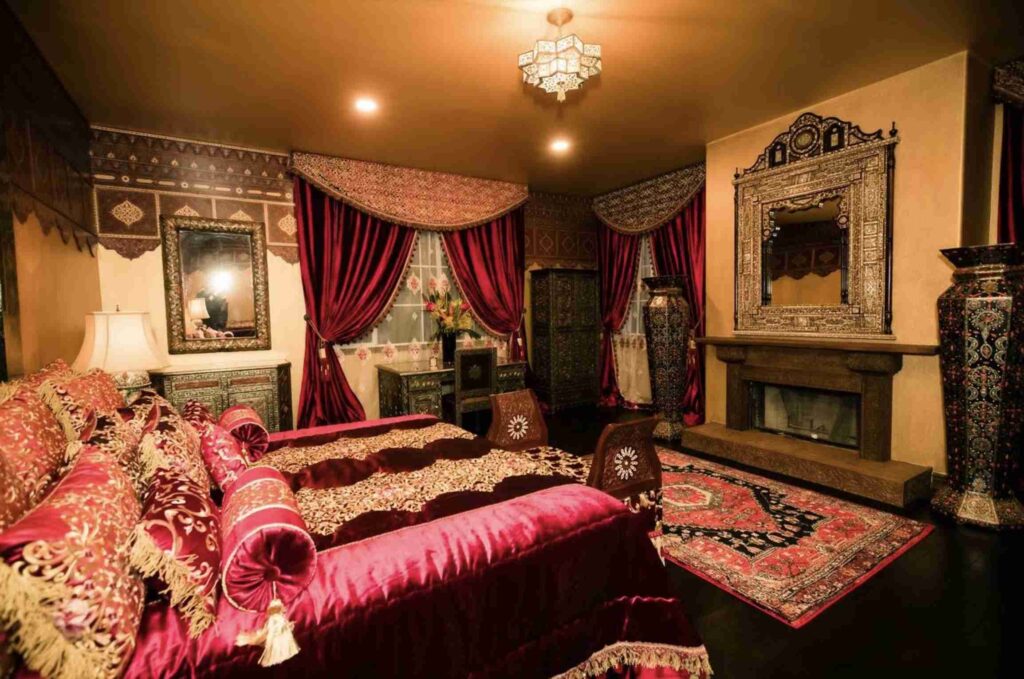 An elaborately decorated room with a Middle Eastern theme, featuring a red velvet sofa, ornate fireplace, intricate rugs, and rich textiles.
