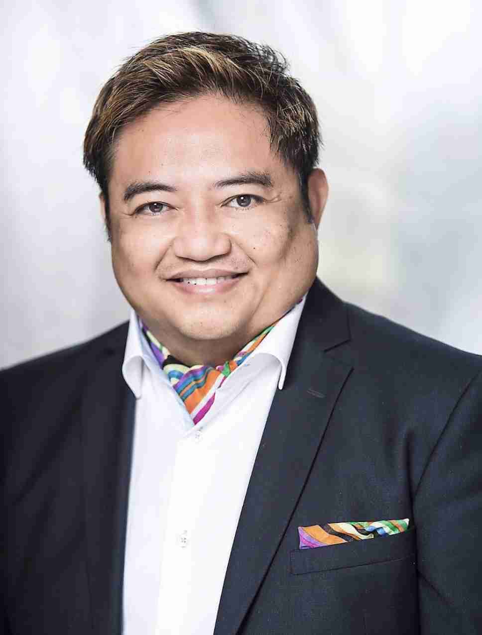 A model is walking down the runway showcasing a vibrant green knit dress with fringe details, accessorized with sunglasses, a necklace, and a handbag.