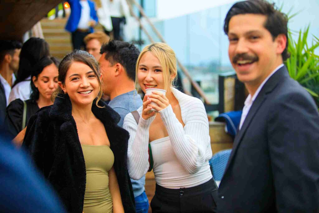A group of people socializing at an outdoor event, with focus on a smiling woman holding a drink.