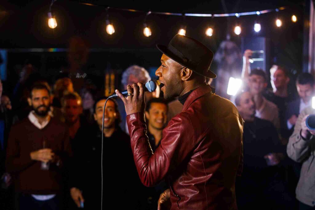 A musician is performing live, singing into a microphone in front of an audience in a dimly lit venue.