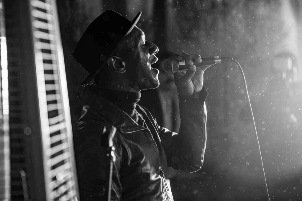 A person is passionately singing into a microphone on stage with dramatic backlighting.