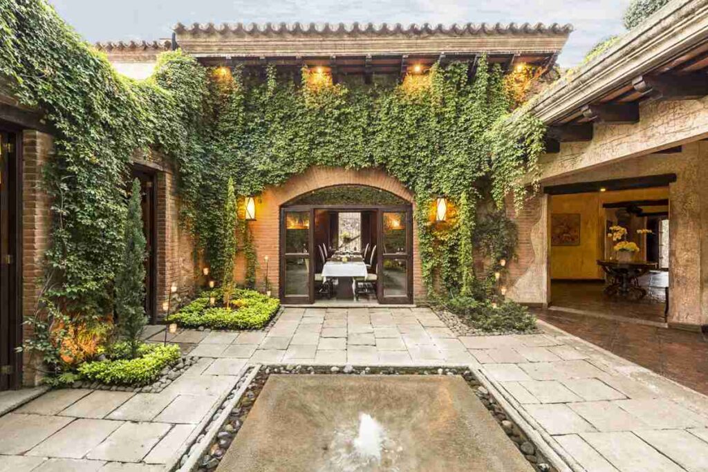 An elegant courtyard with a water feature, surrounded by ivy-covered walls and an inviting dining area under an archway.