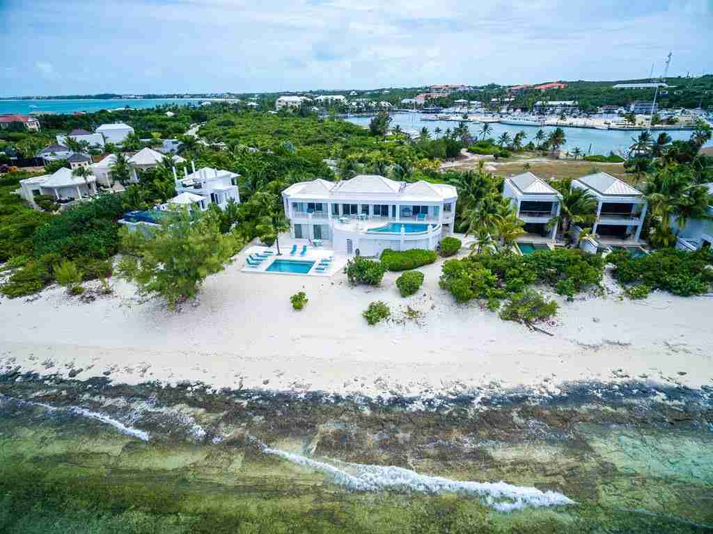 An aerial view of a luxurious coastal property with a pool, adjacent to a sandy beach and turquoise waters.