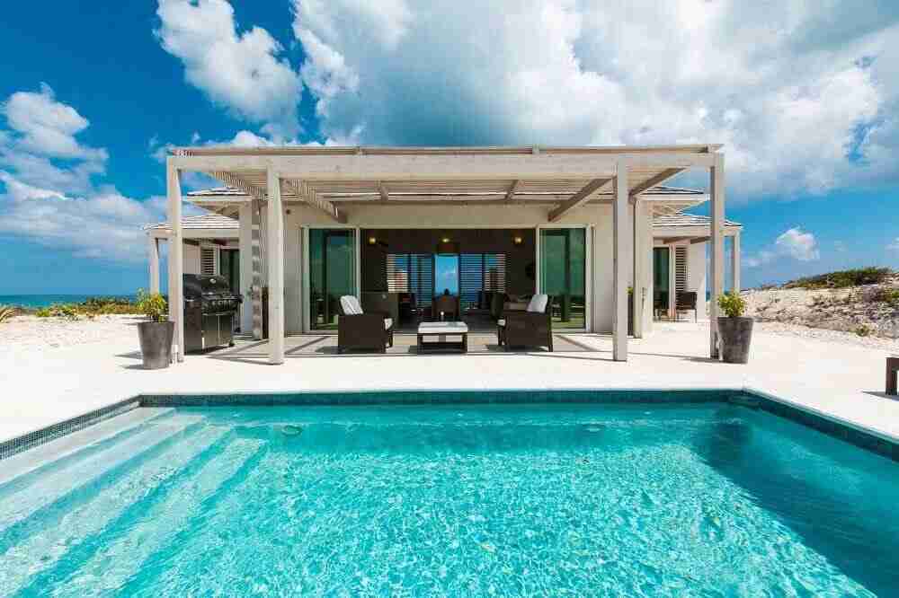 A luxurious beachfront villa with a swimming pool under a clear blue sky.