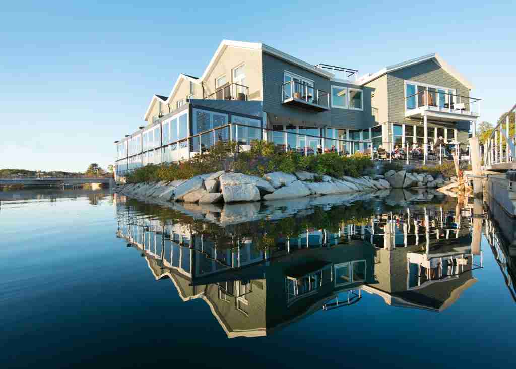 Picture of modern waterfront buildings with clear reflections on a calm body of water under a blue sky.