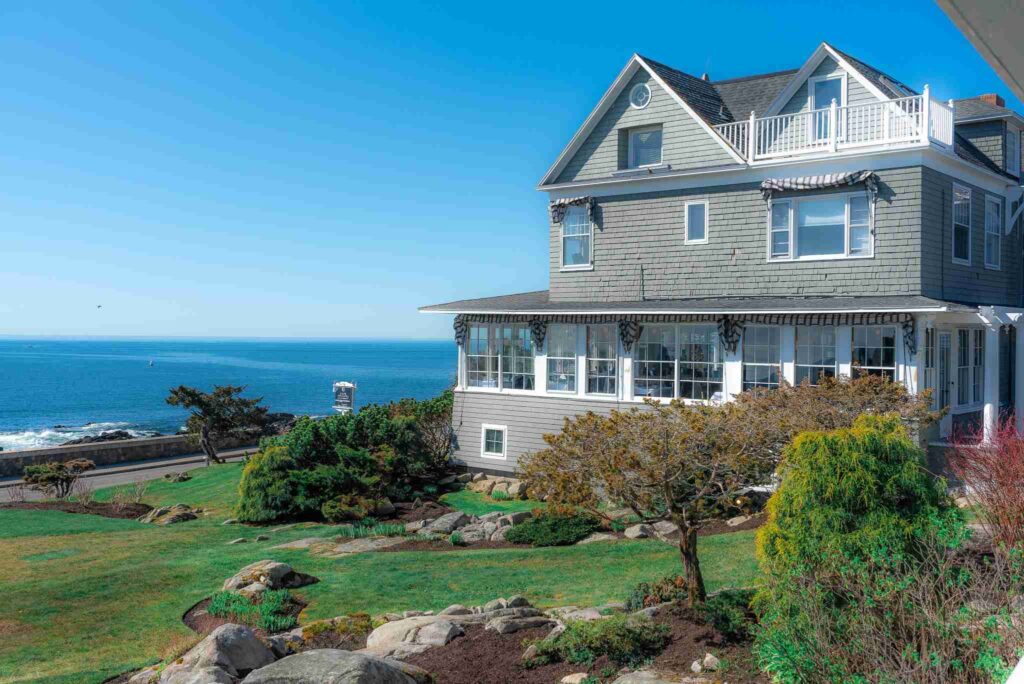 A charming coastal house with a glazed patio overlooking the ocean under a clear blue sky.