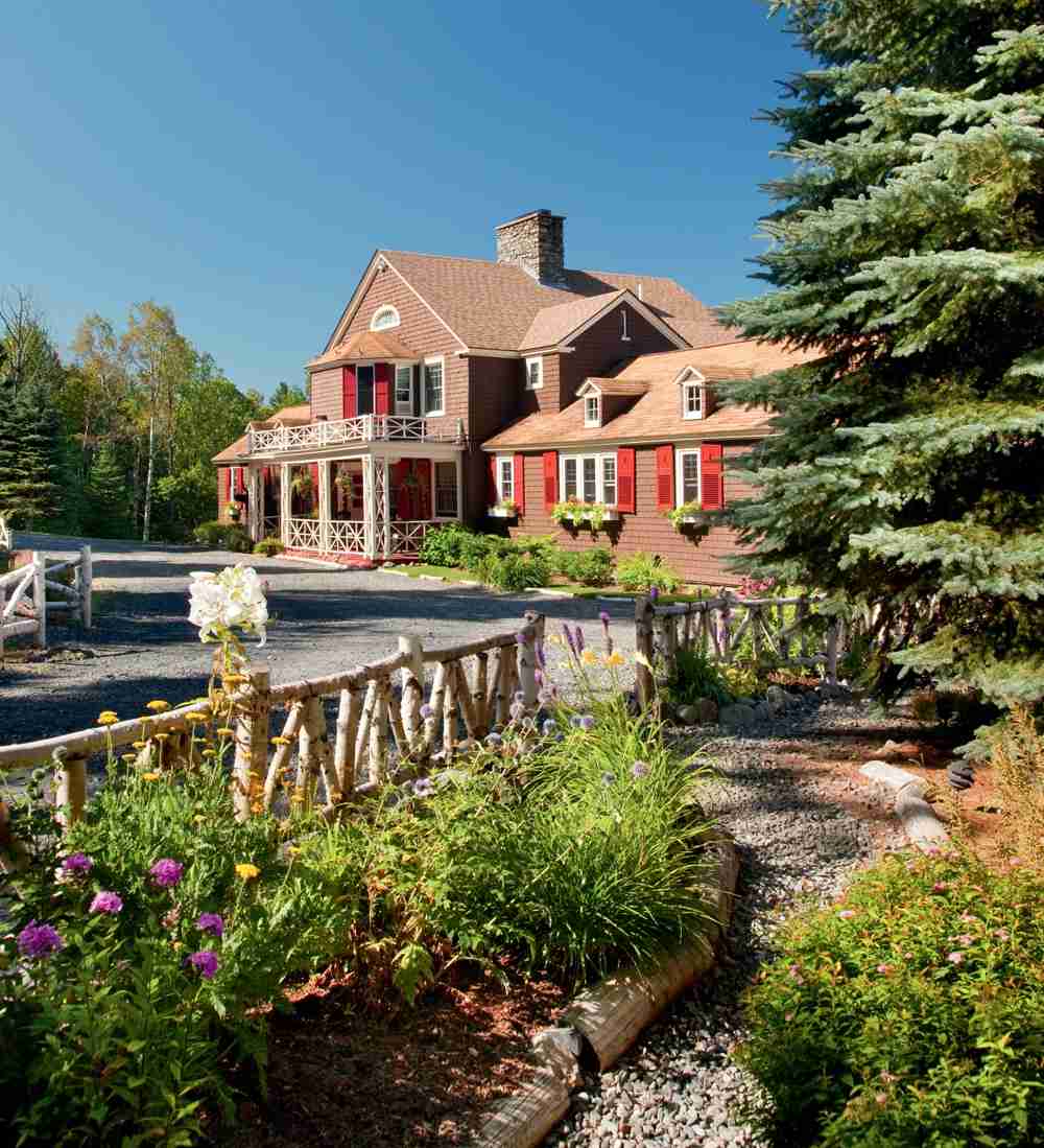 A charming red house with white trimmings surrounded by greenery under a blue sky.