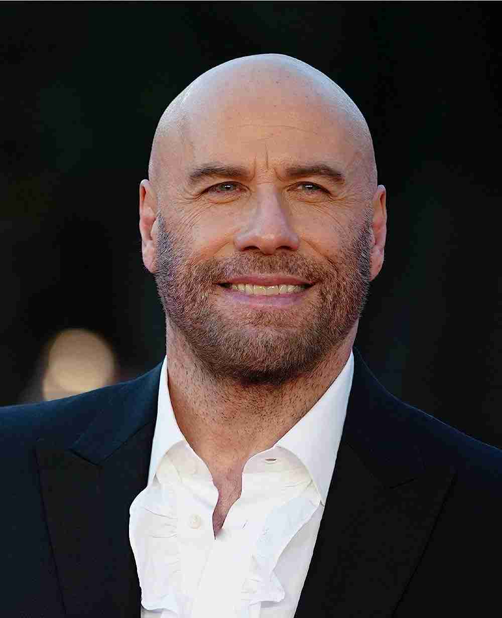 A bald man with a beard, smiling, wearing a black shirt and jacket, against a blurred background.