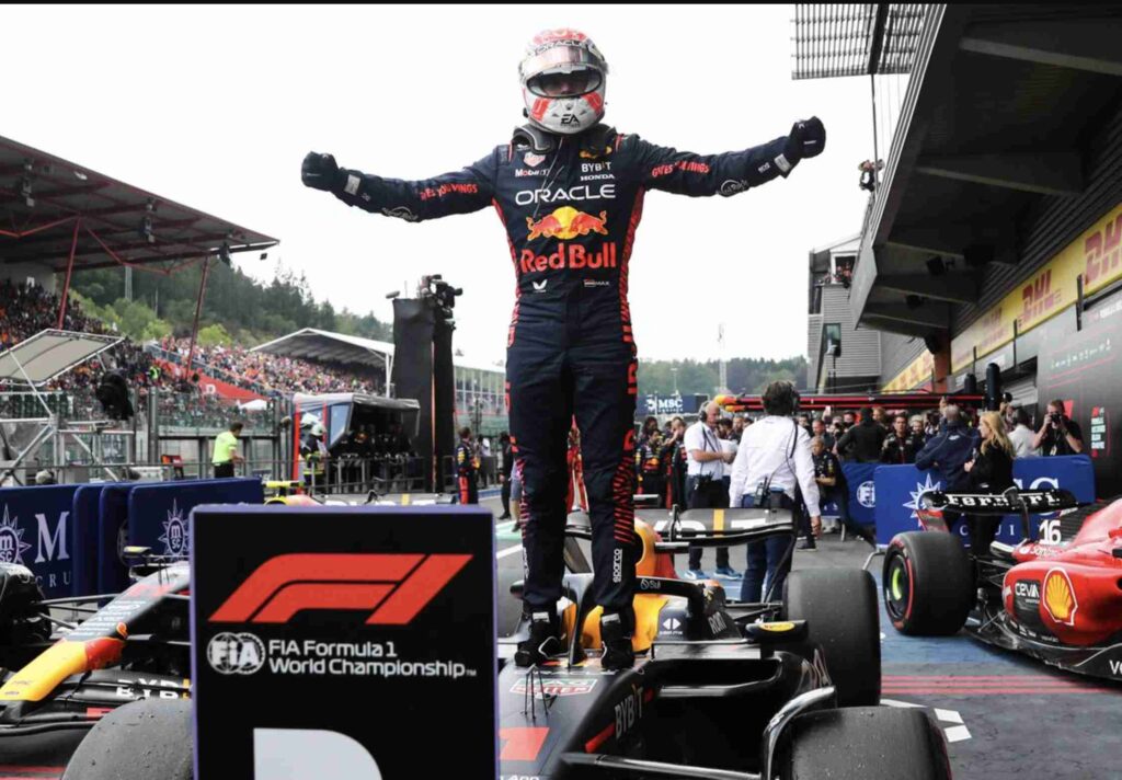 A Formula 1 driver is celebrating on top of a car with the crowd and another racecar in the background.
