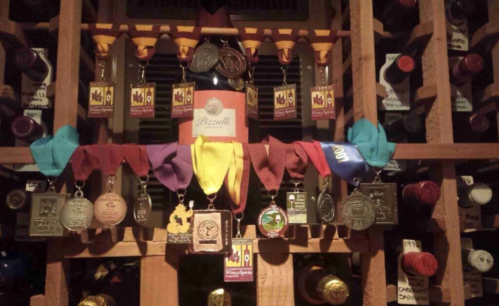 A collection of award-winning wine bottles displayed on wooden shelves adorned with various colorful ribbons and medals.