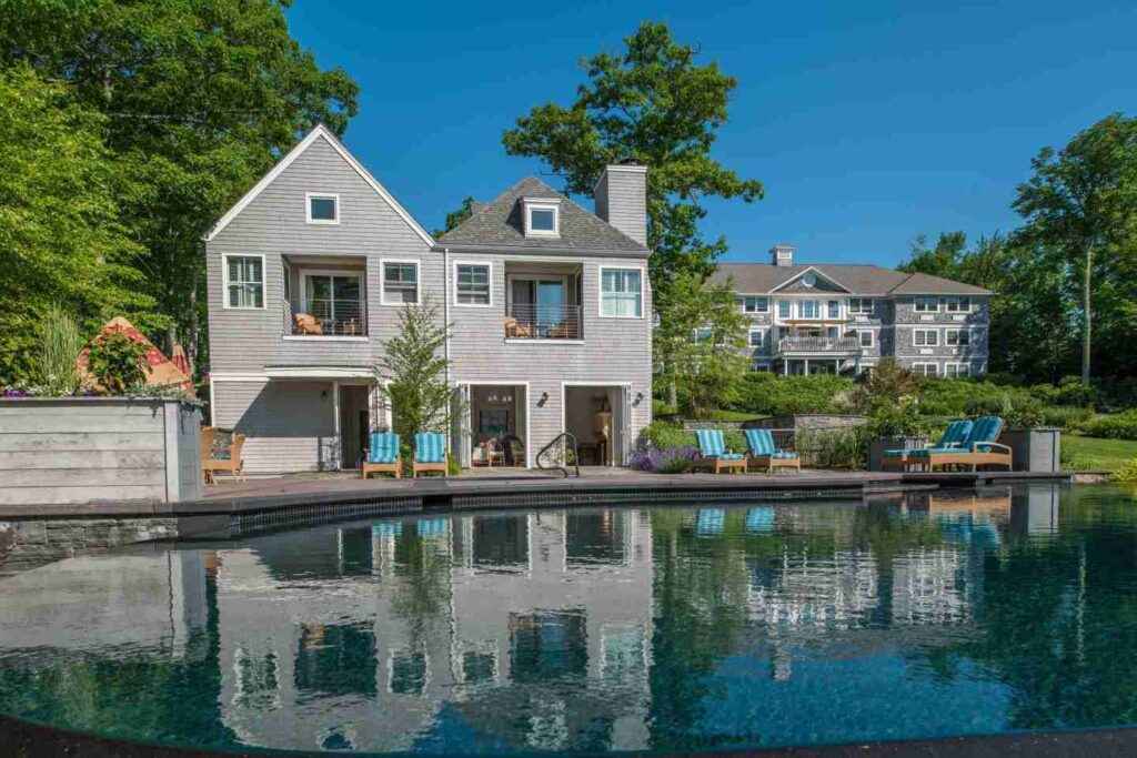 The image shows a two-story suburban home with a large swimming pool in the foreground on a sunny day.