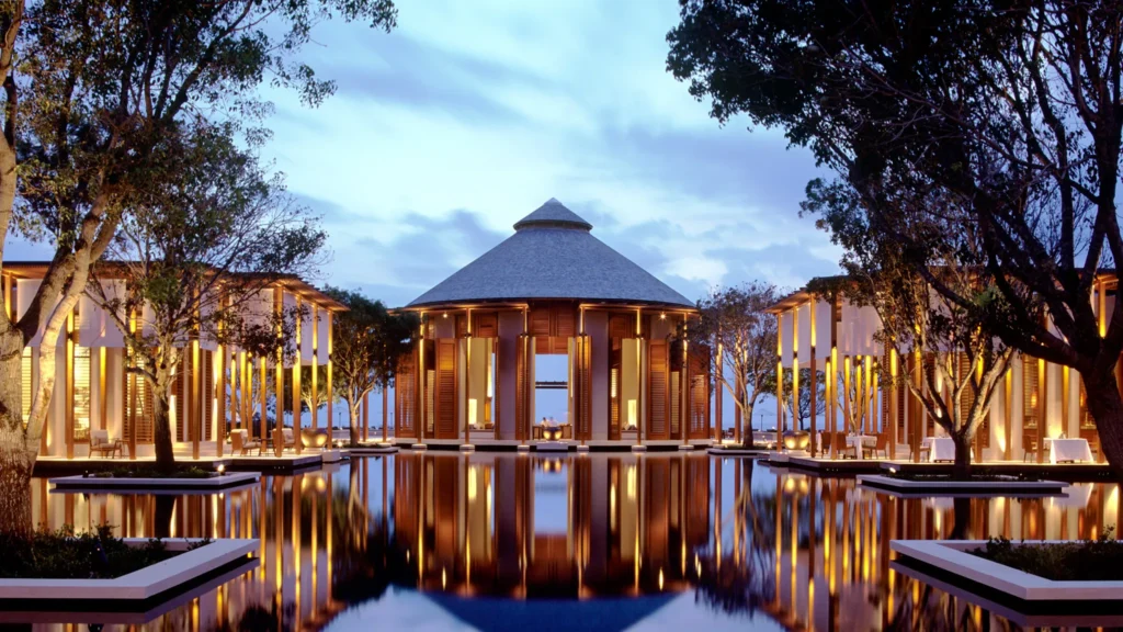 A tranquil luxury resort with a reflective pool at twilight, combining traditional architecture and modern lighting.