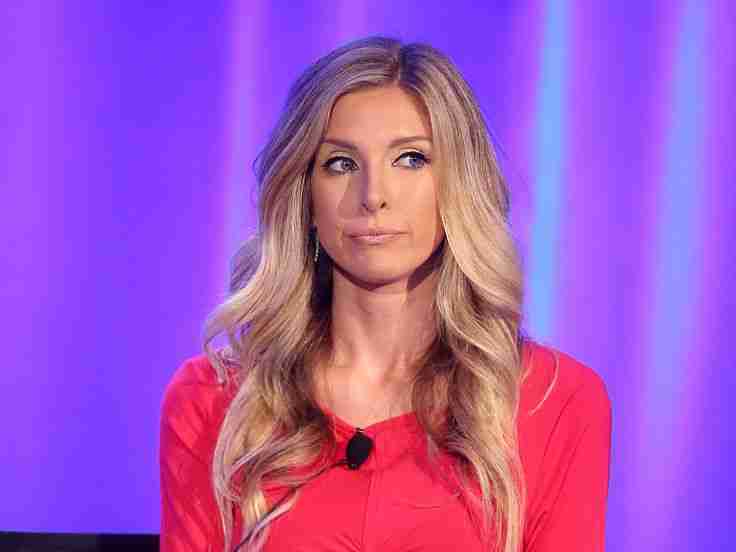 A woman in a red dress with long blonde hair is sitting in front of a purple background.