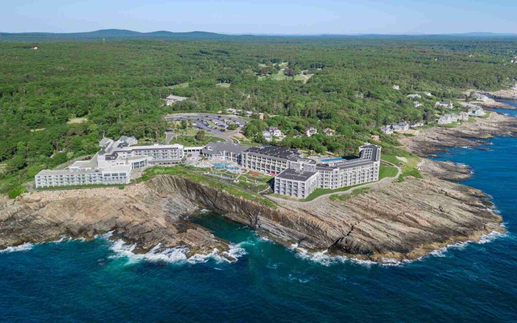 An aerial view of a large coastal resort with multiple buildings situated on a rocky shoreline surrounded by forested land.