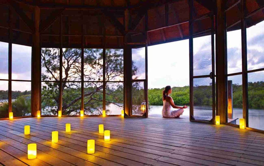 A luxurious room with open sliding doors leading to a beachfront patio with white umbrellas and a serene ocean view.