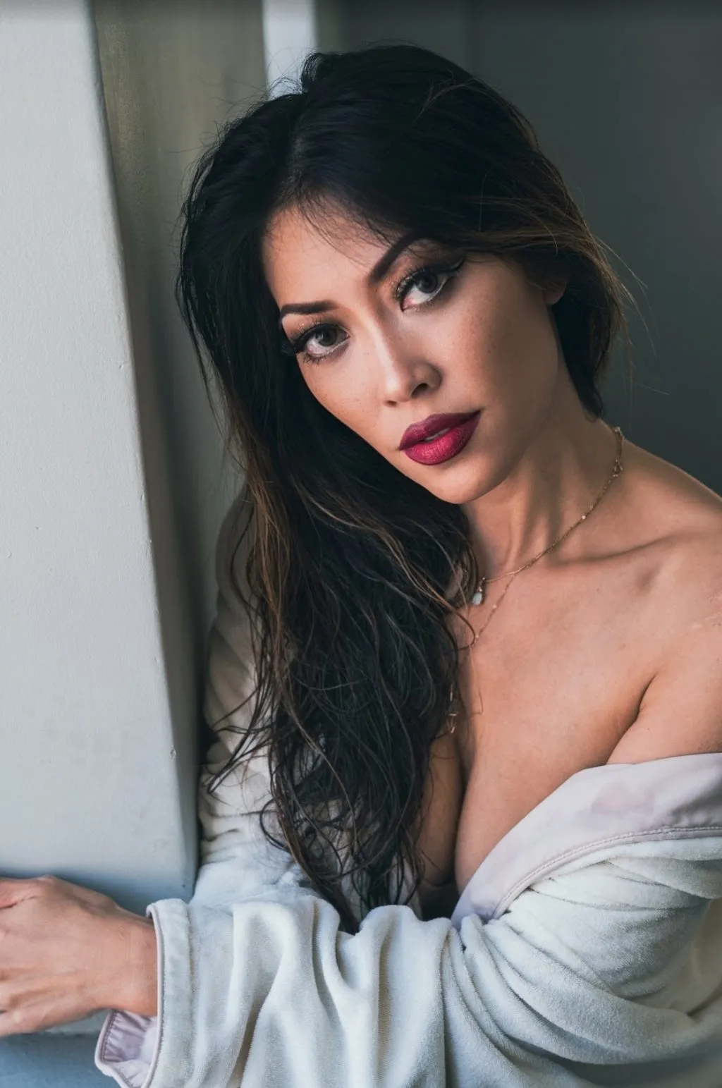 A woman with long dark hair looks over her shoulder with an intense gaze near a blurred foreground element.