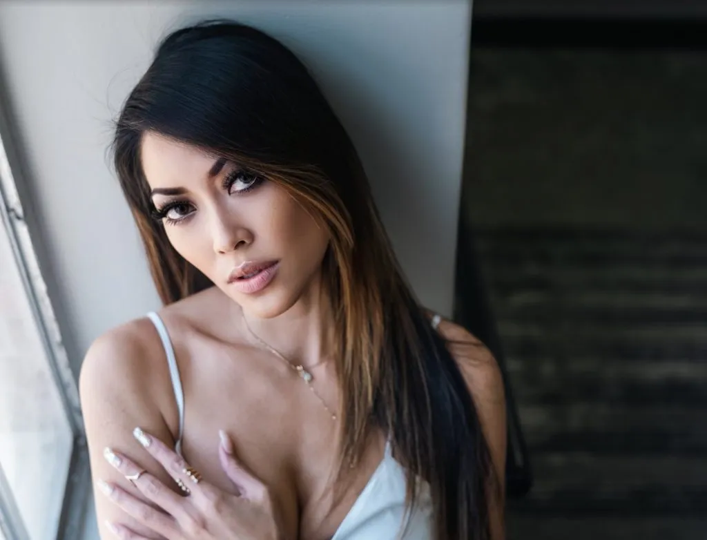 A woman with long dark hair looks over her shoulder with an intense gaze near a blurred foreground element.