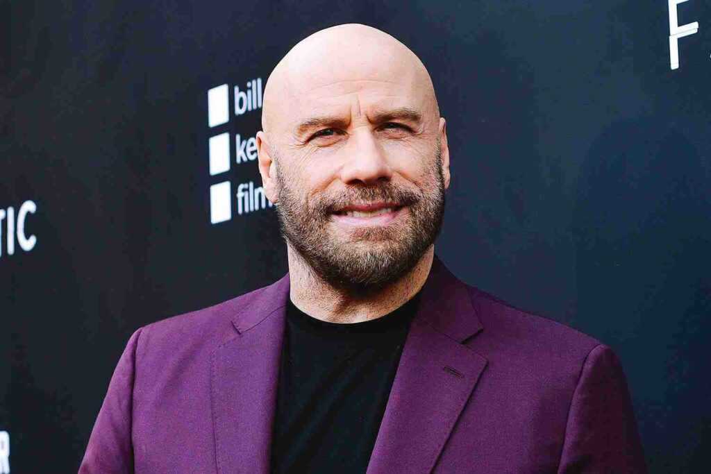 A bald man in a purple suit jacket poses for a photograph on a red carpet event.