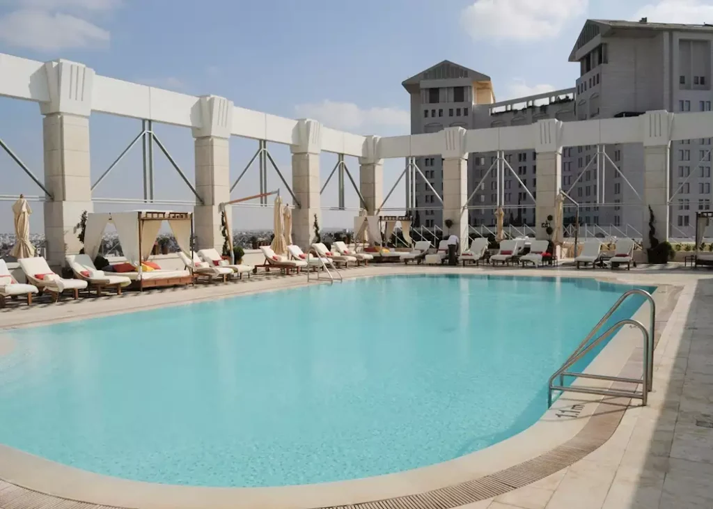 A luxury hotel swimming pool with sun loungers and umbrellas under a clear sky.