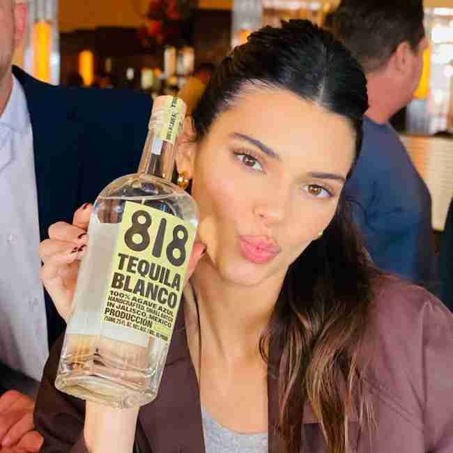 A person posing with a large bottle of 818 Tequila Blanco, making a pouting expression.