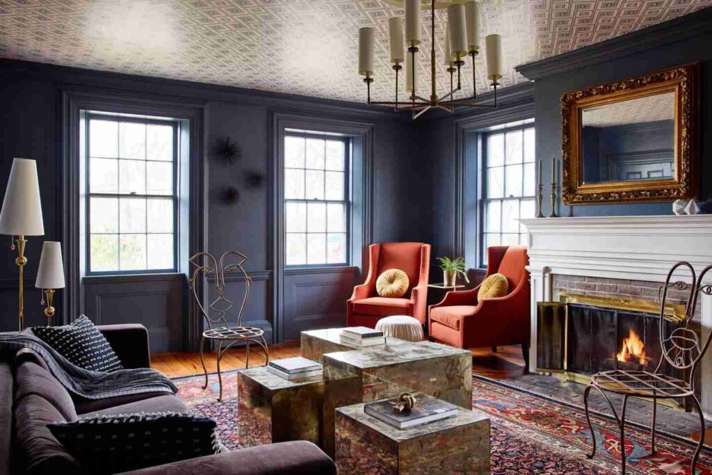 An elegant living room with dark blue walls, a fireplace, plush seating, a patterned rug, and decorative ceiling.