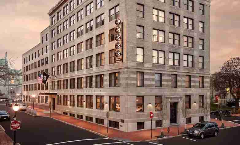 A dusk view of a vintage-style, multi-story corner building with a prominent PRESS sign.