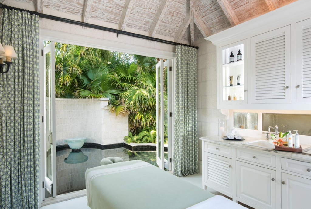 A serene spa room with a massage table, open French doors leading to a lush garden, and tasteful decor fostering a tranquil atmosphere.