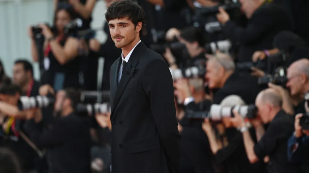 An elegant dining room with white tablecloths, red chairs, chandeliers, large windows, and ornate decor.
