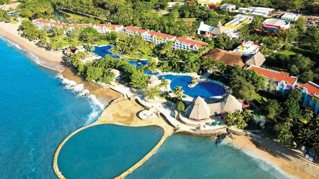 An elegant dining room with white tablecloths, red chairs, chandeliers, large windows, and ornate decor.