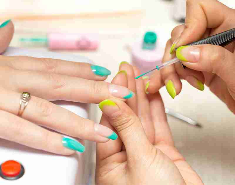 A person is applying green nail polish on someone's nails during a manicure with various nail care tools and polishes visible.