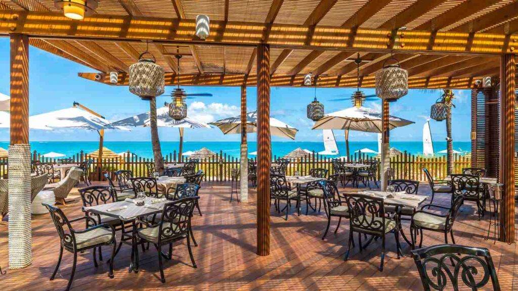 An elegant dining room with white tablecloths, red chairs, chandeliers, large windows, and ornate decor.