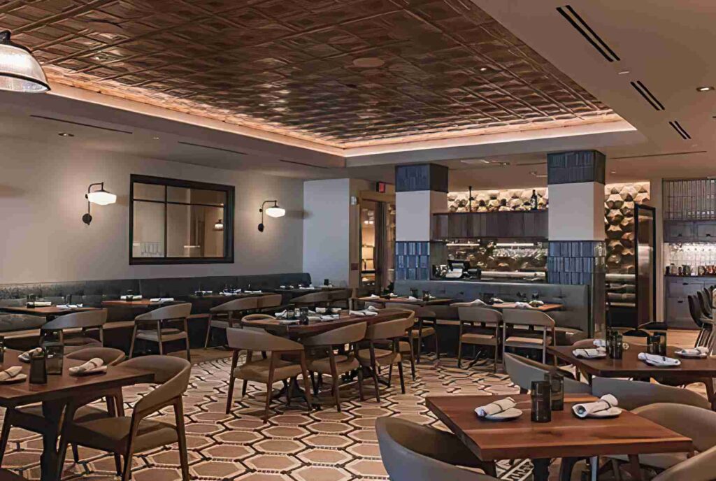 An elegant dining area with tables set for service, decorative lighting, patterned flooring, and a visible bar area in the background.