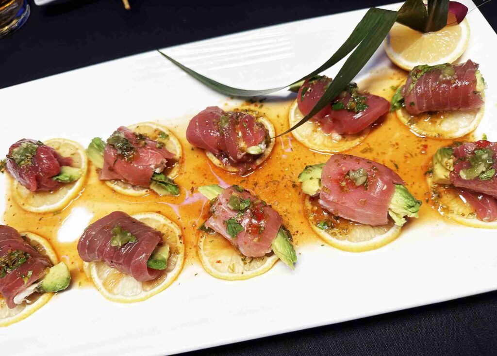 A group of people is smiling and toasting with drinks at a bar with blue lighting.