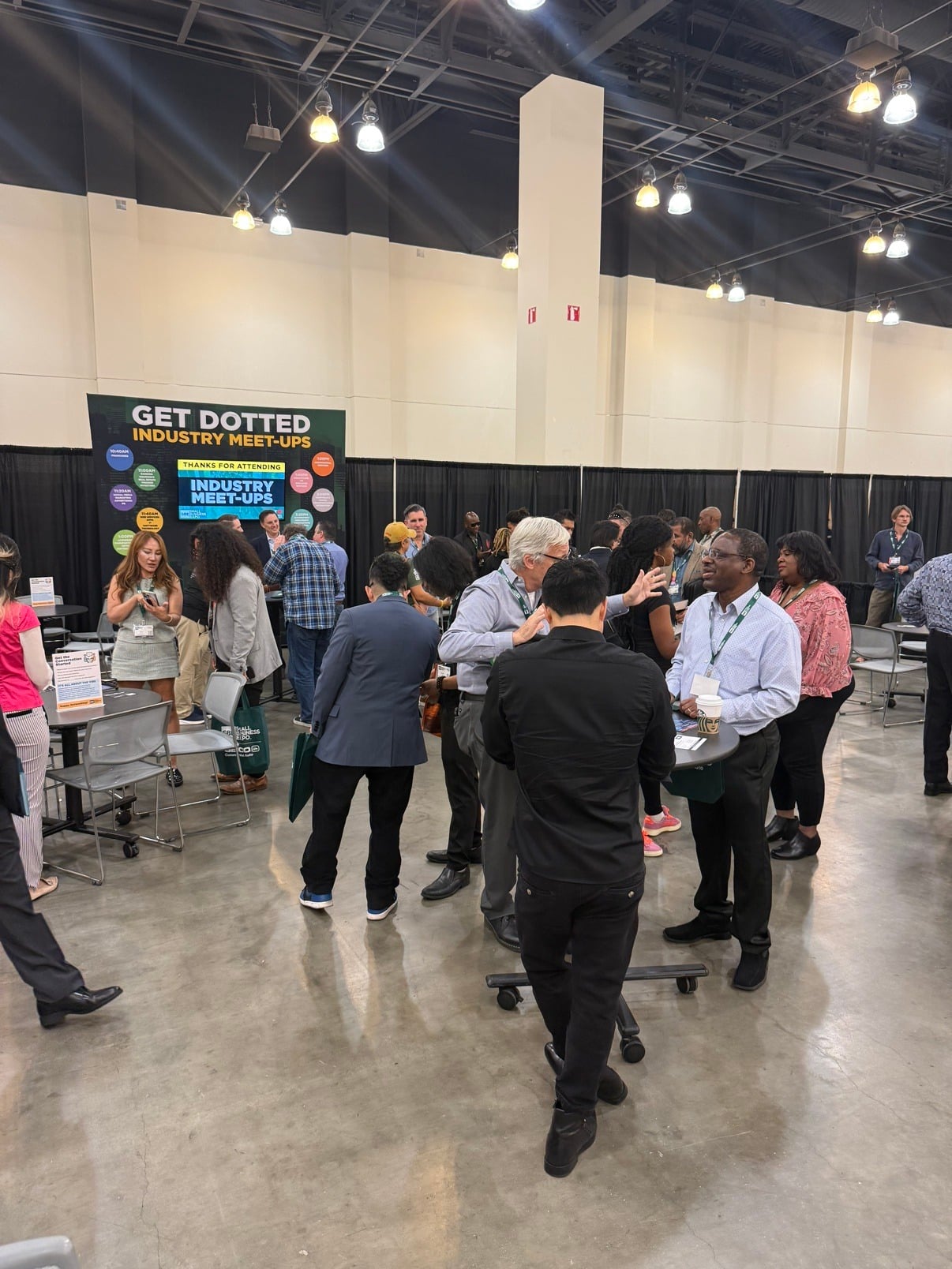 Attendees networking at the Industry Meet-Ups area on the expo floor at Small Business Expo Los Angeles 2026 at the Pasadena Convention Center, beneath a large overhead sign reading Get Dotted Industry Meet-Ups, with franchise and art and entertainment meetup signs visible.