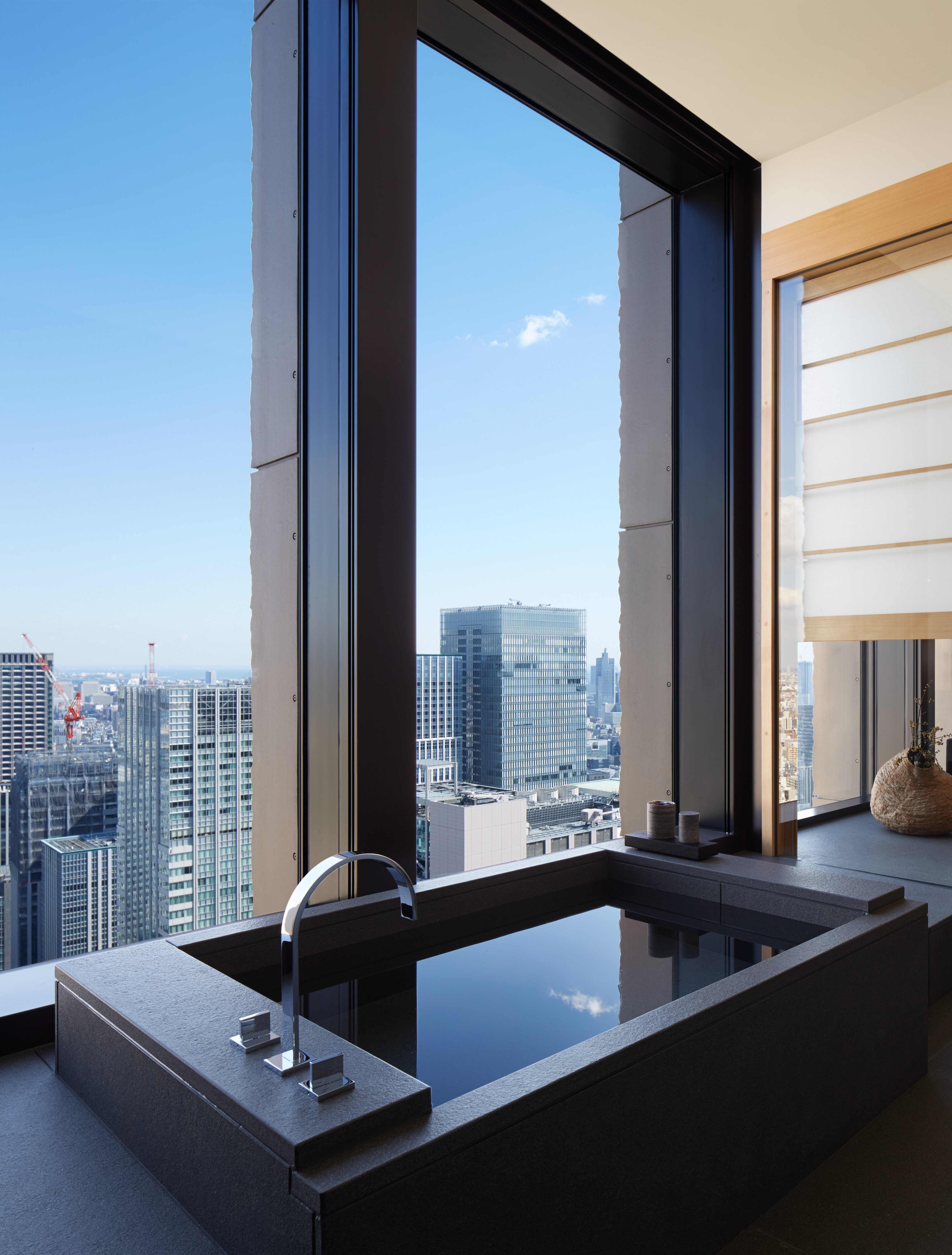 Aman Tokyo suite bathroom with a deep stone furo soaking tub beside floor-to-ceiling windows overlooking the Tokyo skyline