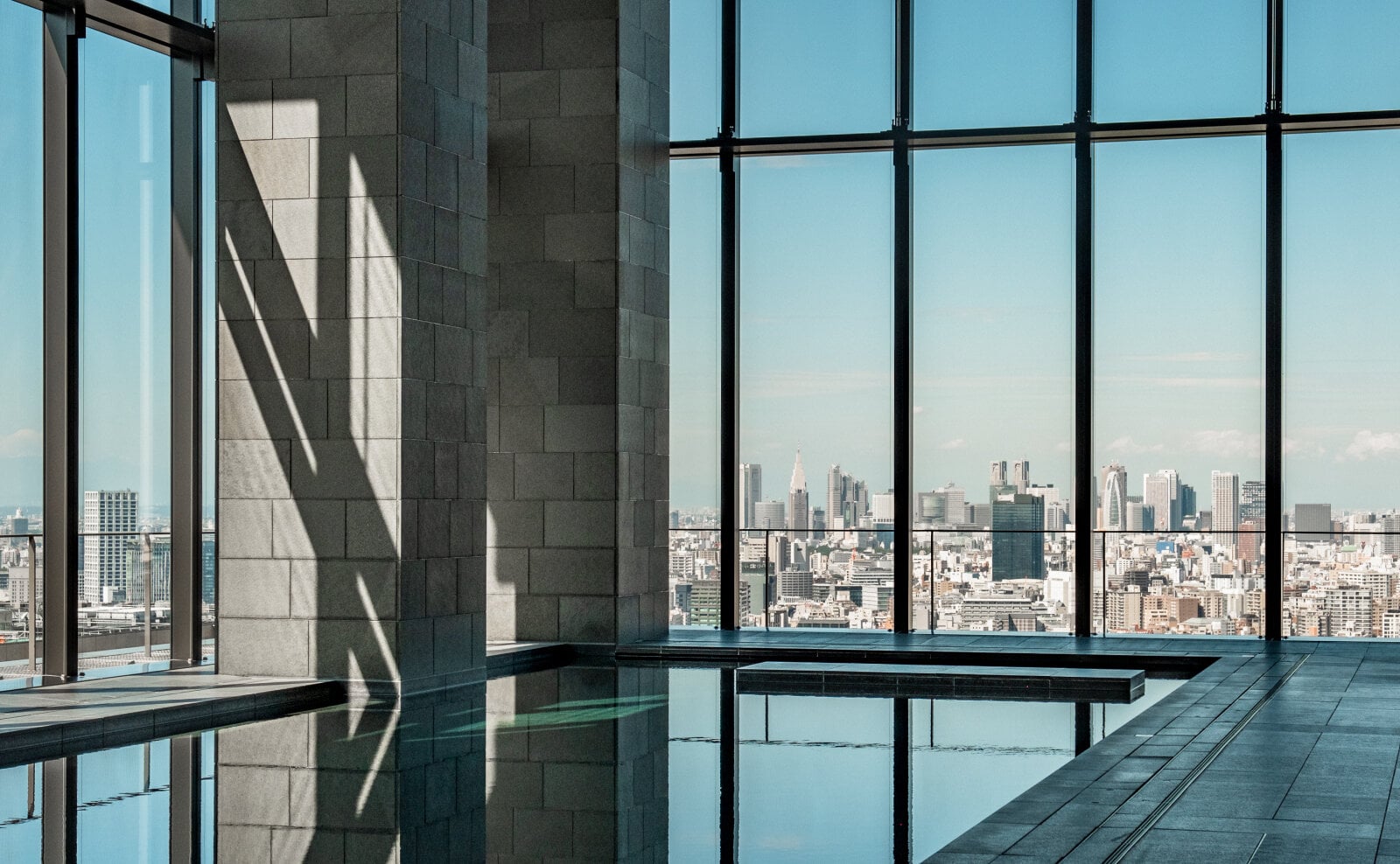 Aman Tokyo 30-metre indoor swimming pool with stone columns and floor-to-ceiling windows overlooking the Tokyo skyline