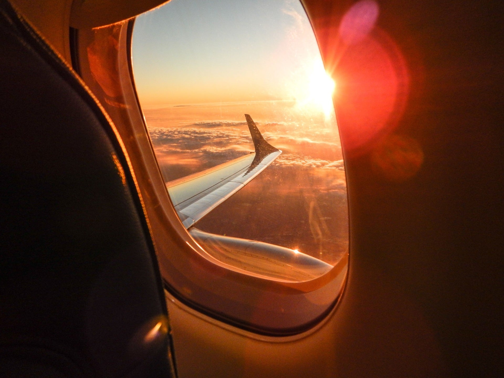 Airplane wing above the clouds viewed from a passenger window at sunset