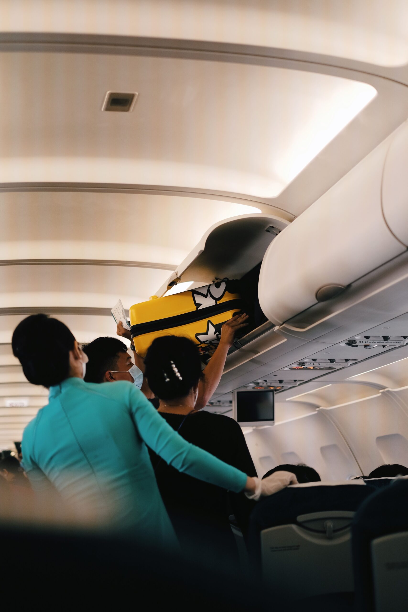 Passenger placing a yellow carry-on suitcase in an airplane overhead bin