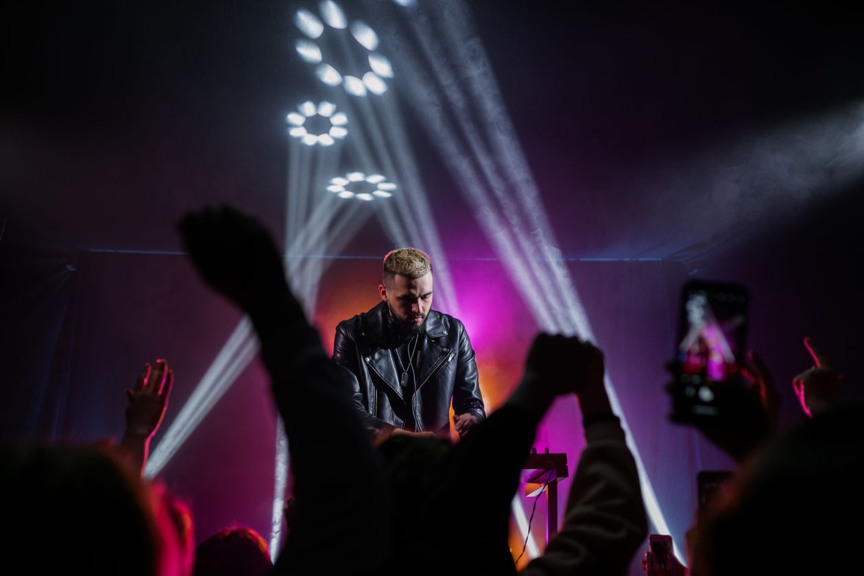 DJ performing live on stage with dramatic colorful lighting in front of an excited crowd at a high-end party