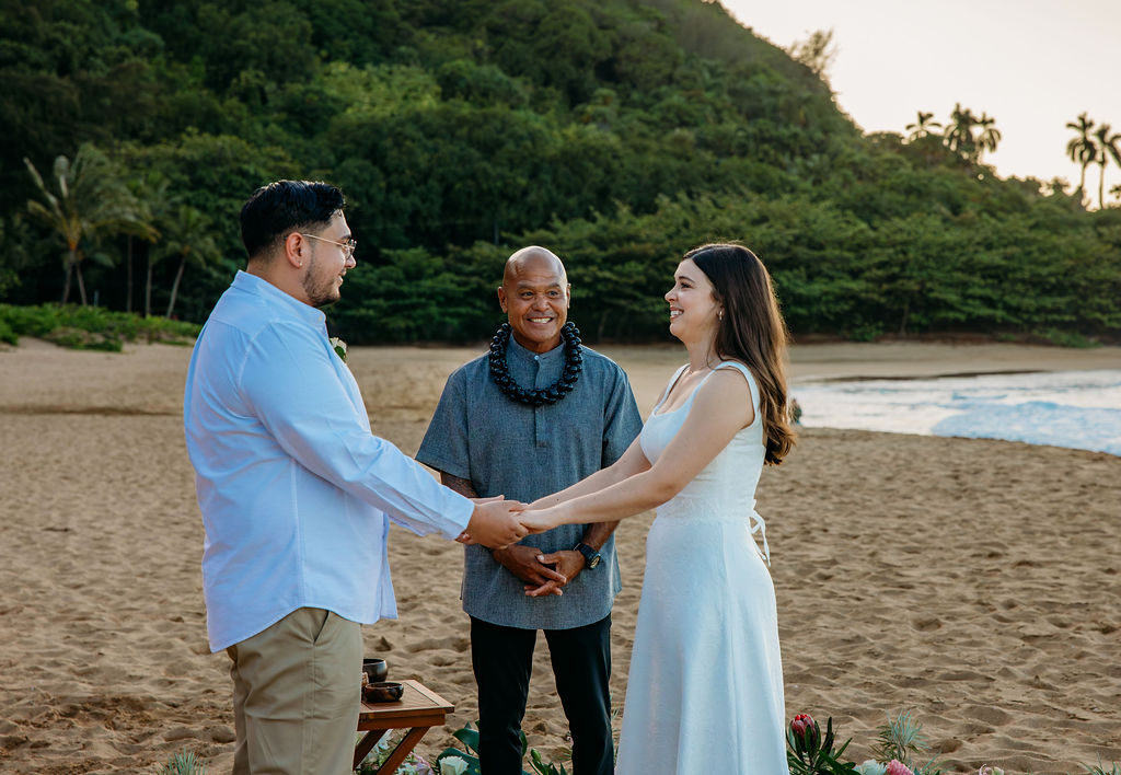 Couple holding hands during an outdoor beach wedding ceremony at sunset