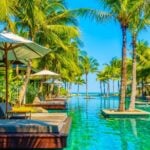 Palm-lined resort pool leading to the ocean at a tropical island resort.