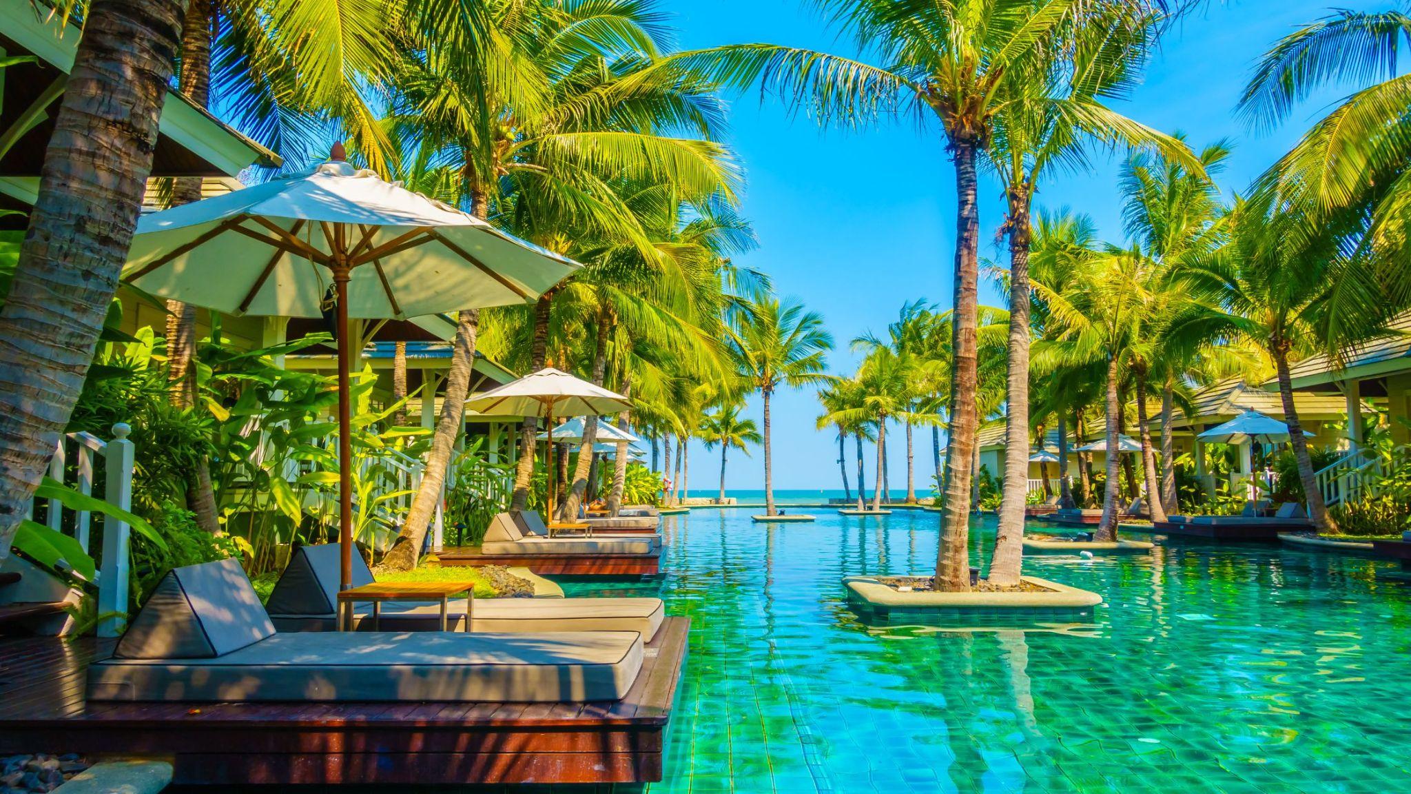 Palm-lined resort pool leading to the ocean at a tropical island resort.