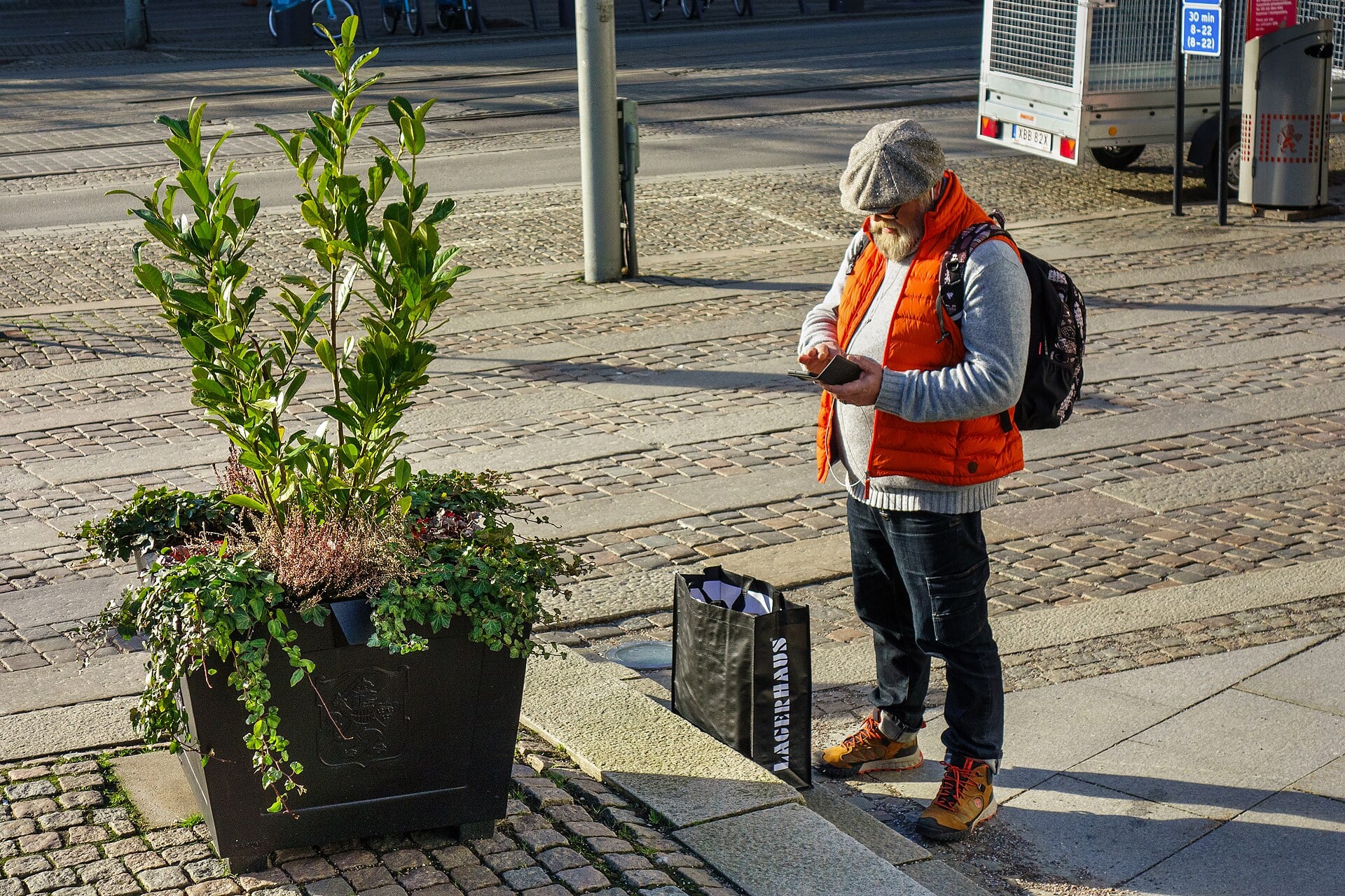 A traveler in an orange vest checking his smartphone on a cobblestone street in Gothenburg, Sweden