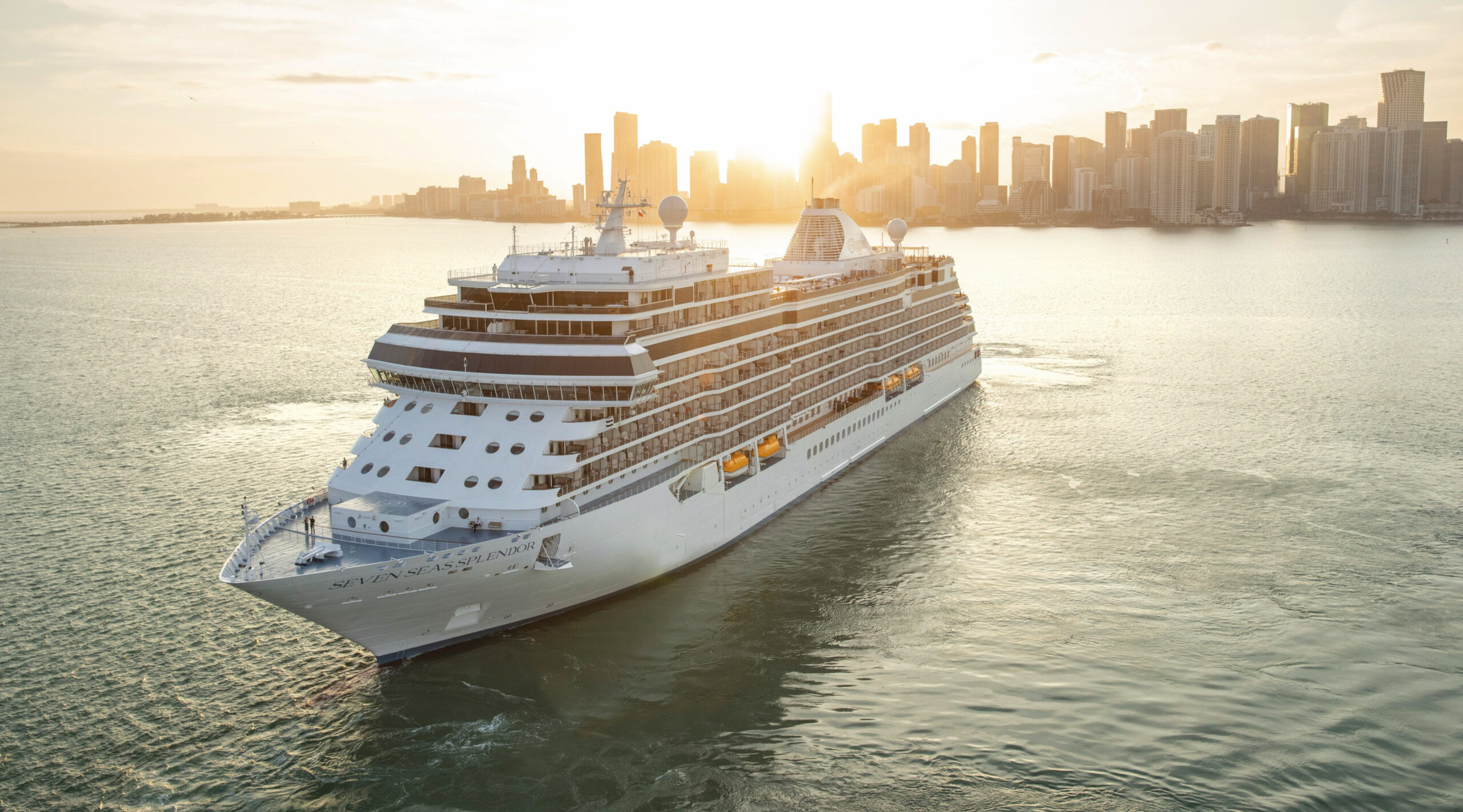 The Seven Seas Splendor luxury cruise ship sailing past the Miami skyline at sunset