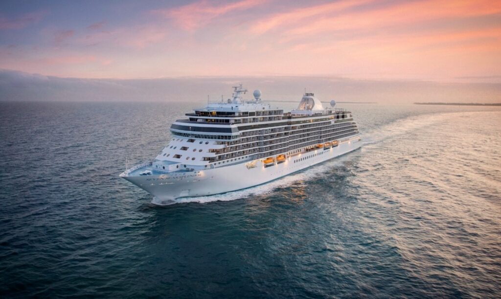 The Seven Seas Splendor cruise ship sailing on open ocean under a colorful sunset sky