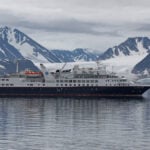 Small expedition cruise ship in polar waters with snow-capped mountains