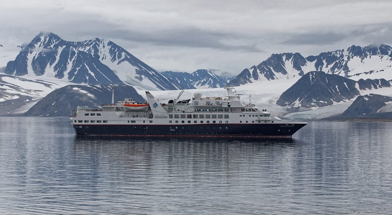 Small expedition cruise ship in polar waters with snow-capped mountains